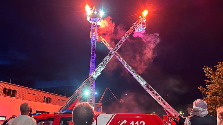 Brennende Fackeln tanzen auf ausgefahrenen Drehleitern bei der Nacht der offenen Tür der Feuerwehr Reutlingen. 